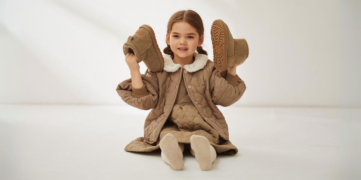 A girl is holding a pair of UGG kids boots in olive colour