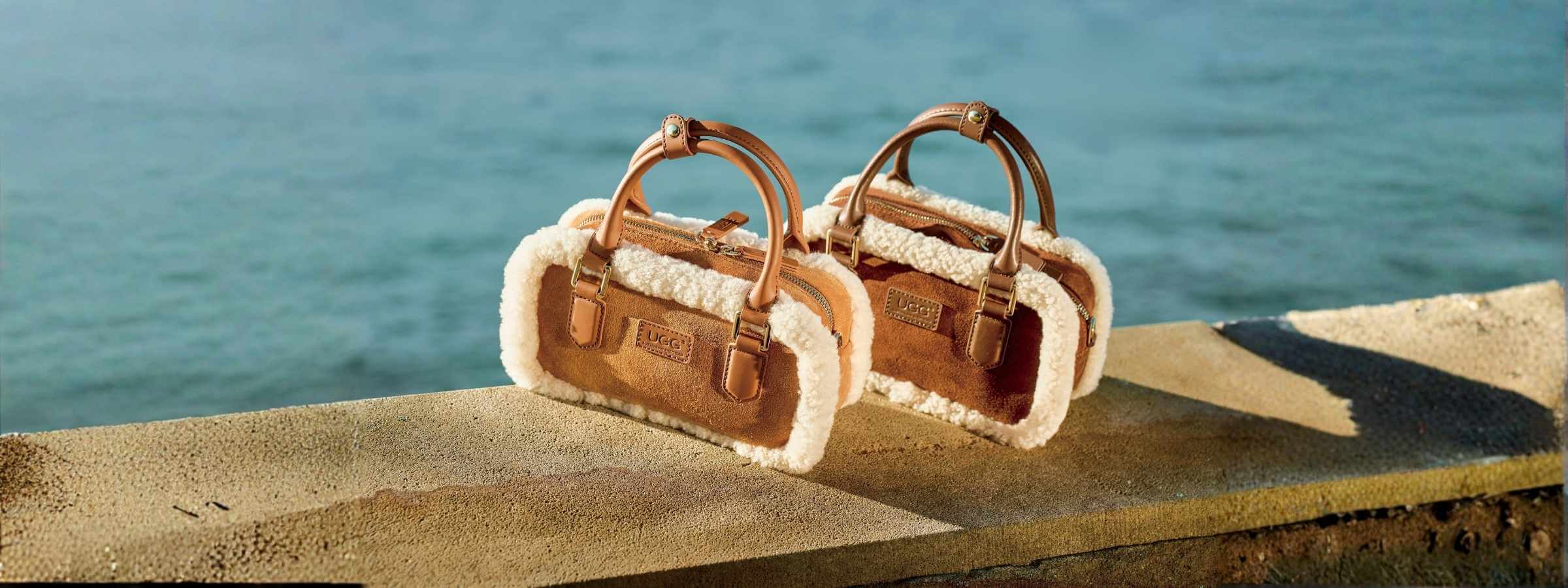 Luxury UGG handbags in tan suede with shearling trim, photographed by the sea — shop the latest UGG bags collection at Peroz Australia.
