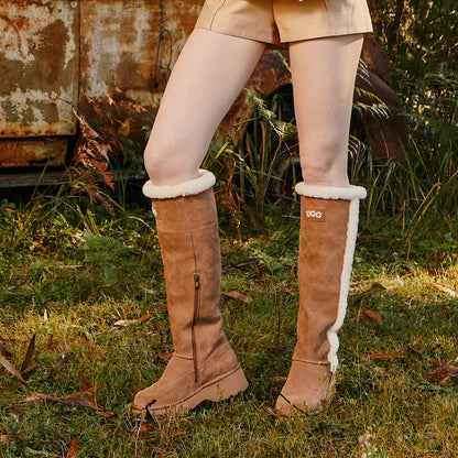 Brown knee-high UGG boots with white fur trim worn by a women in a natural setting.