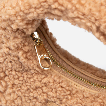 Close-up of a beige shearling bag with a gold zipper and &